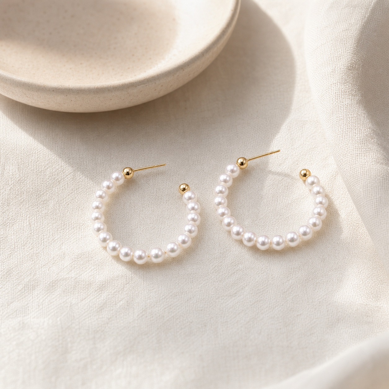 Gold-tone Pearl Hoop Earrings styled on cream linen